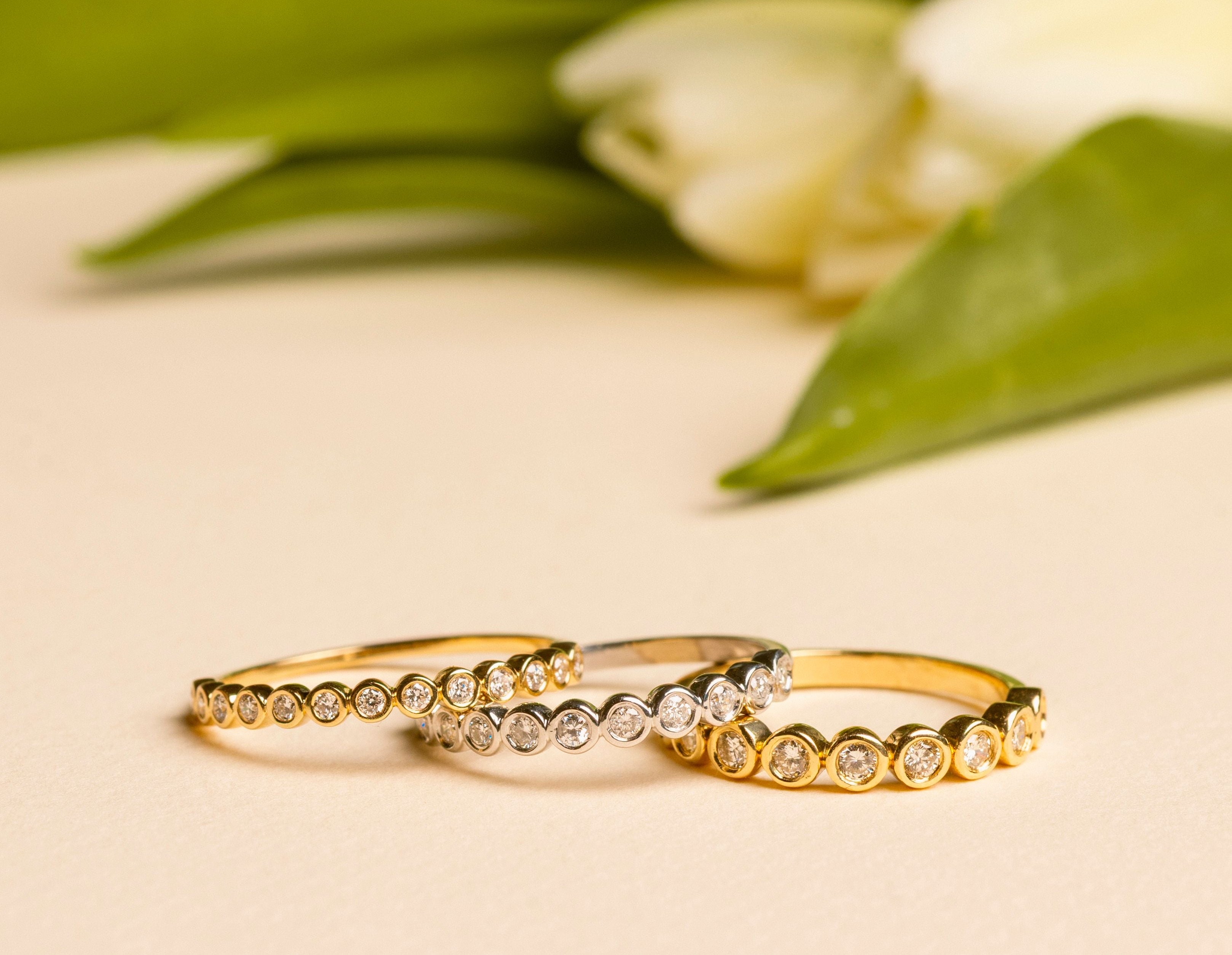 Three gold rings with diamonds on a light background with green leaves and flowers.