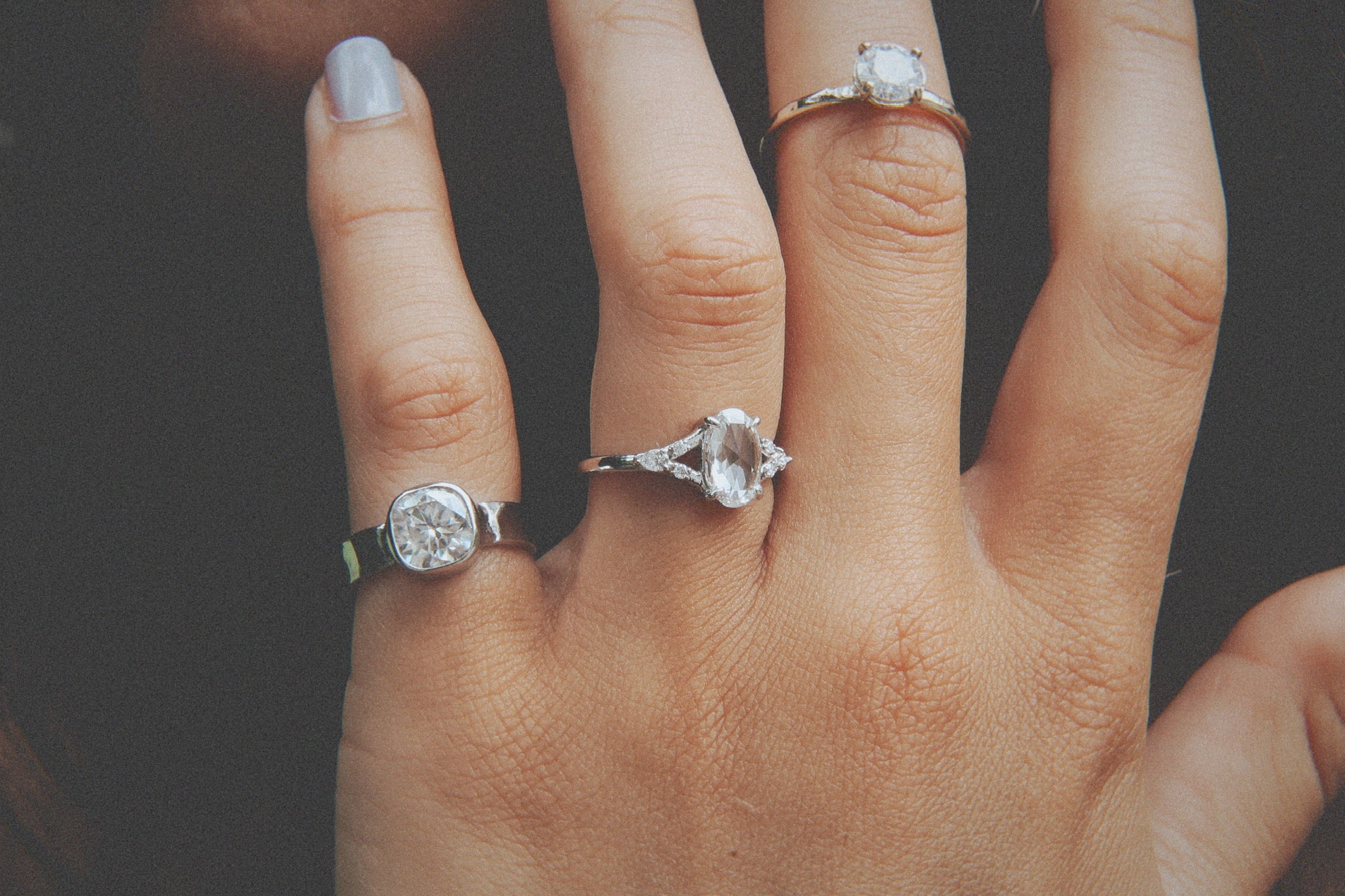 Close-up of a hand wearing two diamond rings on a dark background