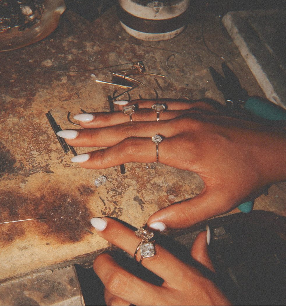Close-up of hands with rings on a jewelry-making workbench.